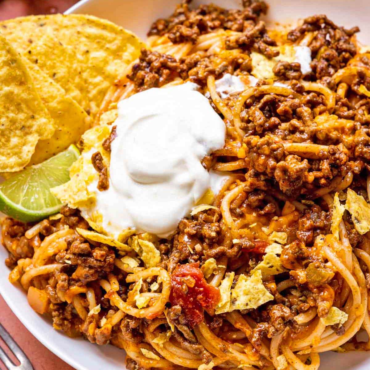 Taco Spaghetti finished pasta dish in bowl with chips, lime, and sour cream garnish