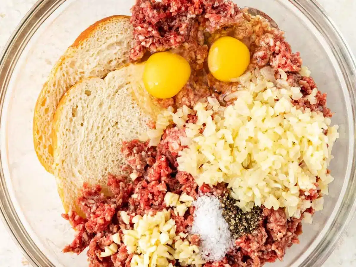 Ground meat, eggs, garlic, bread, and seasonings in bowl.