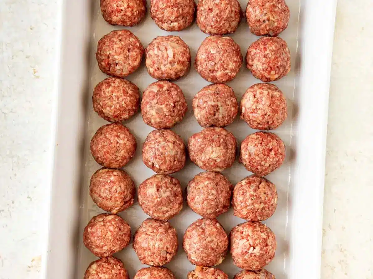 Raw ground meat formed into balls in baking pan.