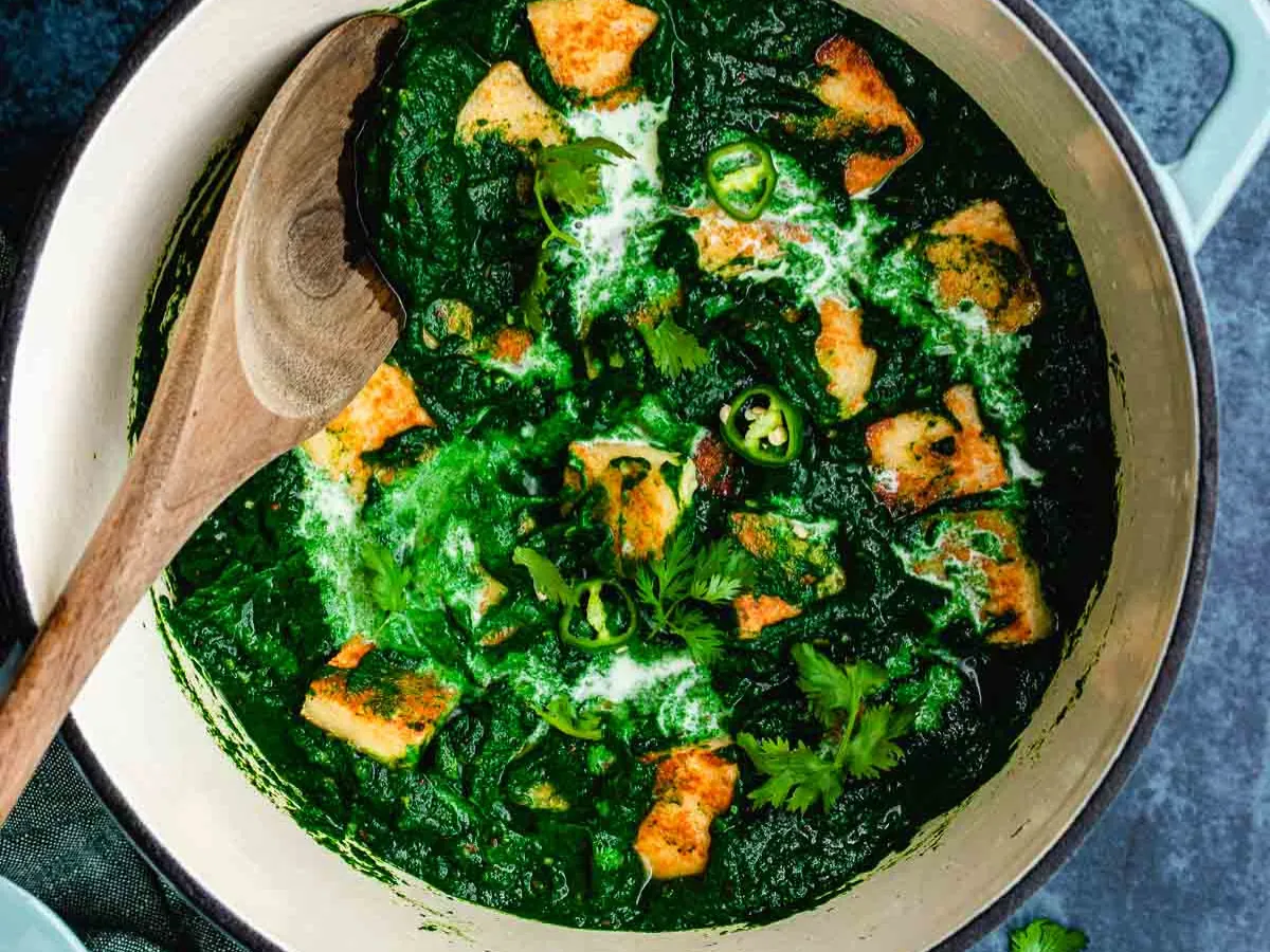 Firm cheese cubes in pot with spinach gravy.