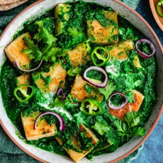 Large bowl with paneer cubes in a spinach gravy.