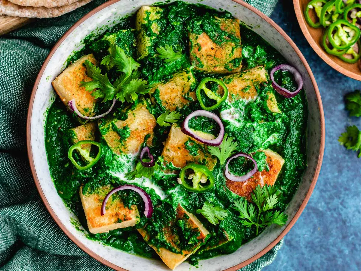 Large bowl with paneer cubes in a spinach gravy.