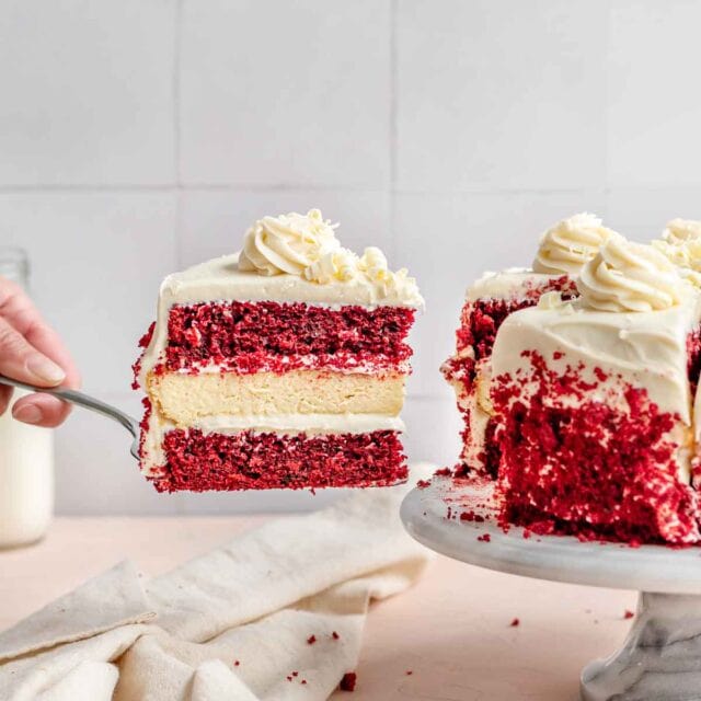 Red Velvet Cheesecake Cake slice on cake server next to cake on cake plate, 1x1 image ratio