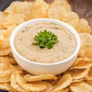 Dip finished in a bowl with green onions on top and bowl surrounded by potato chips on platter, 4x3