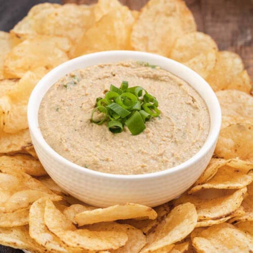Dip finished in a bowl with green onions on top and bowl surrounded by potato chips on platter, 4x3