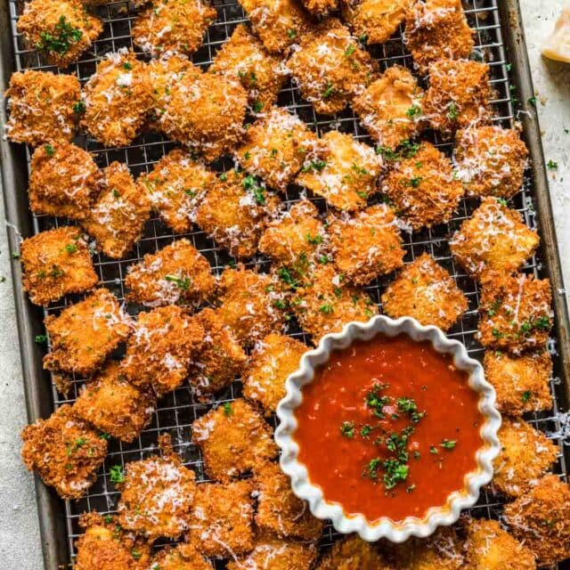 Fried Ravioli cooked ravioli on wire rack with parsley and cheese garnish with bowl of marinara sauce