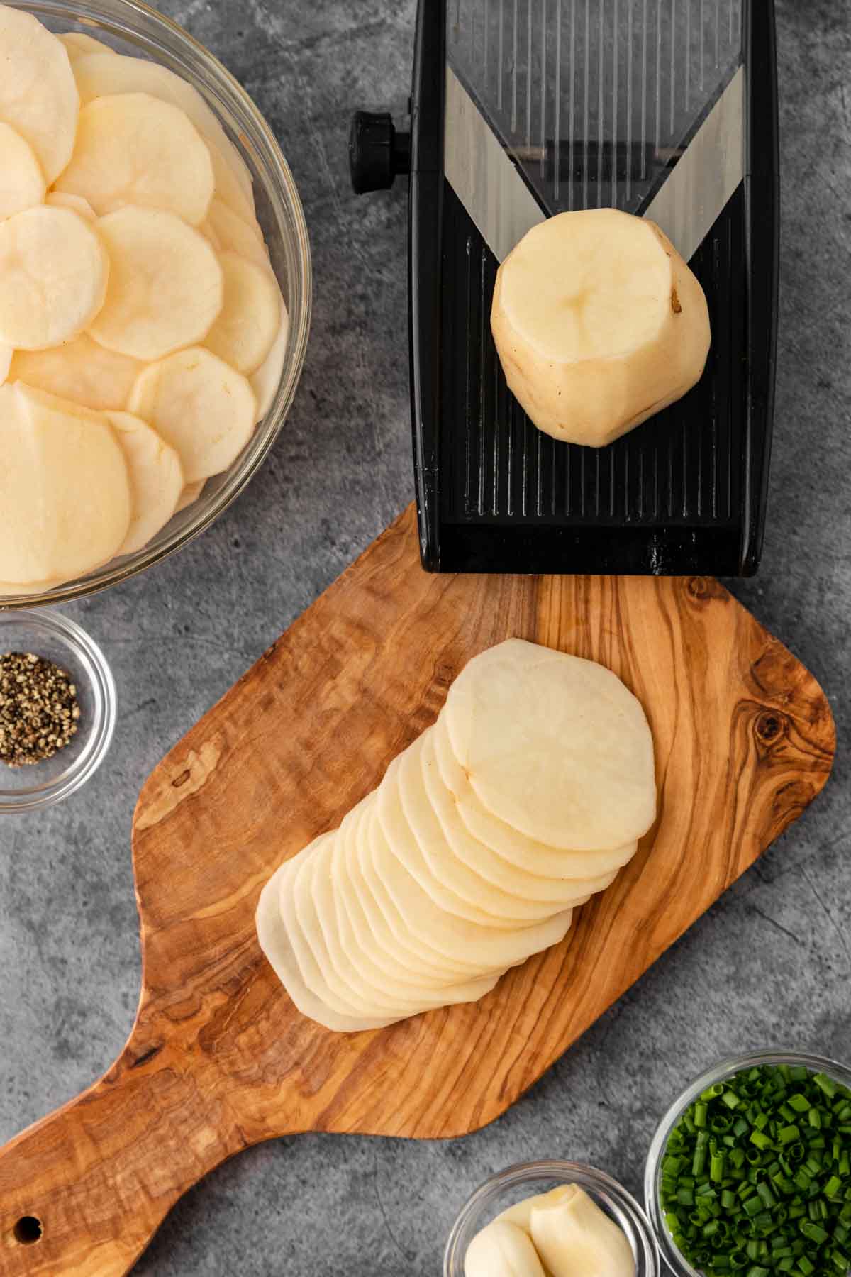Potato Gratin Dauphinois slices of potato on cutting board with mandoline and slices in bowl.