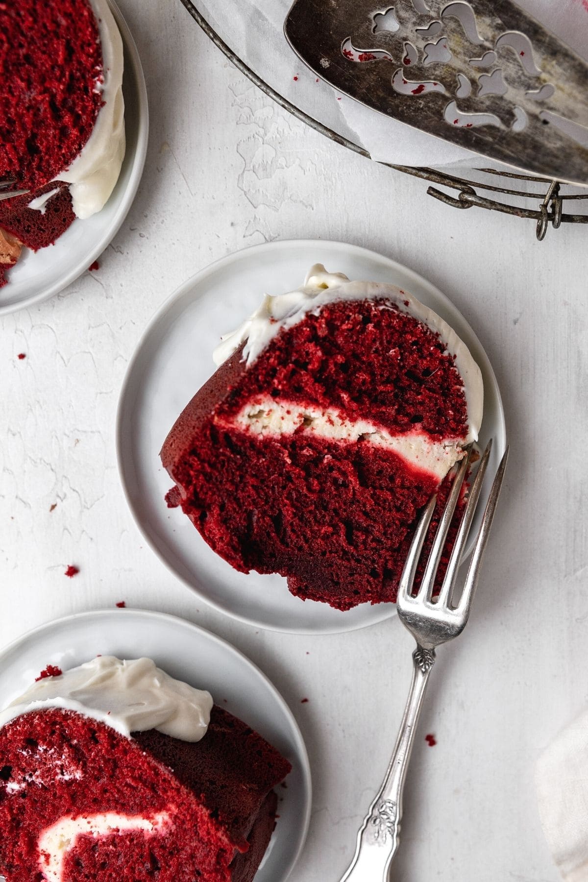 Red Velvet Cheesecake Bundt Cake frosted cake slice laying on plate with fork
