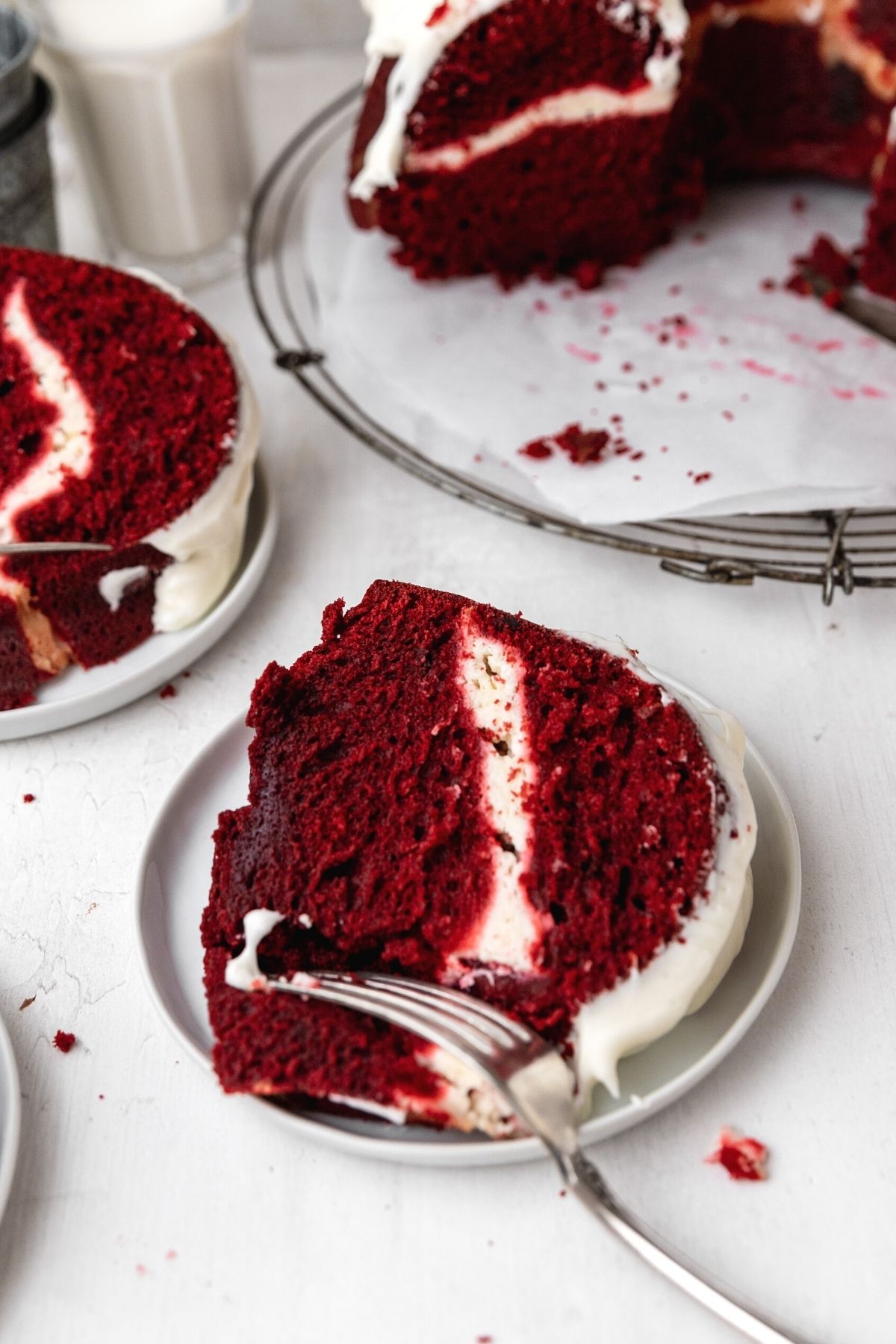 Red Velvet Cheesecake Bundt Cake frosted cake slice laying on plate with fork cutting bite