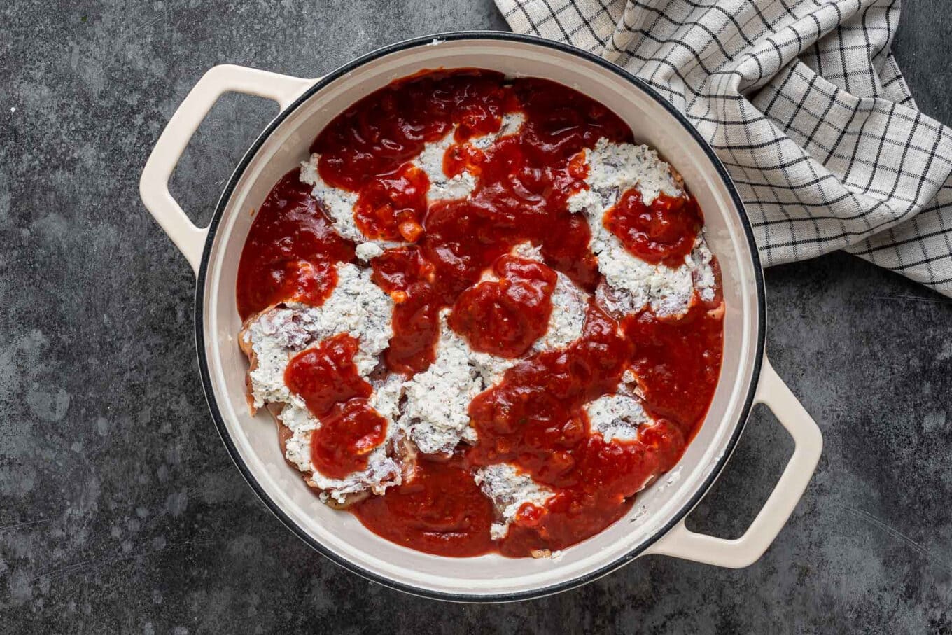 boneless chicken thighs covered with cheese mixture and sauce in Dutch oven before baking