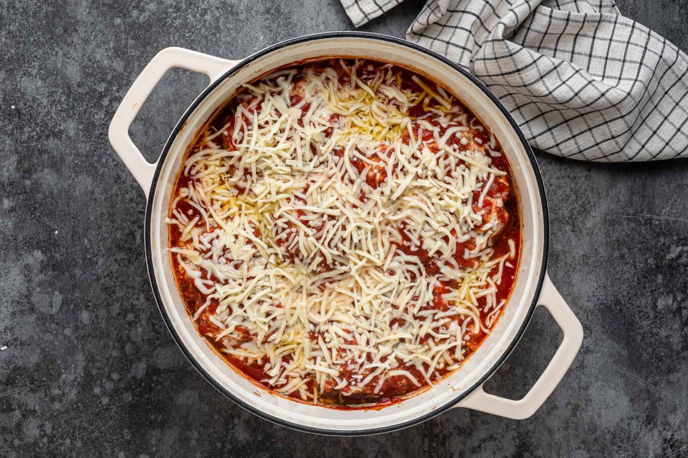cooked chicken and sauce covered in shredded cheese before melting in Dutch oven