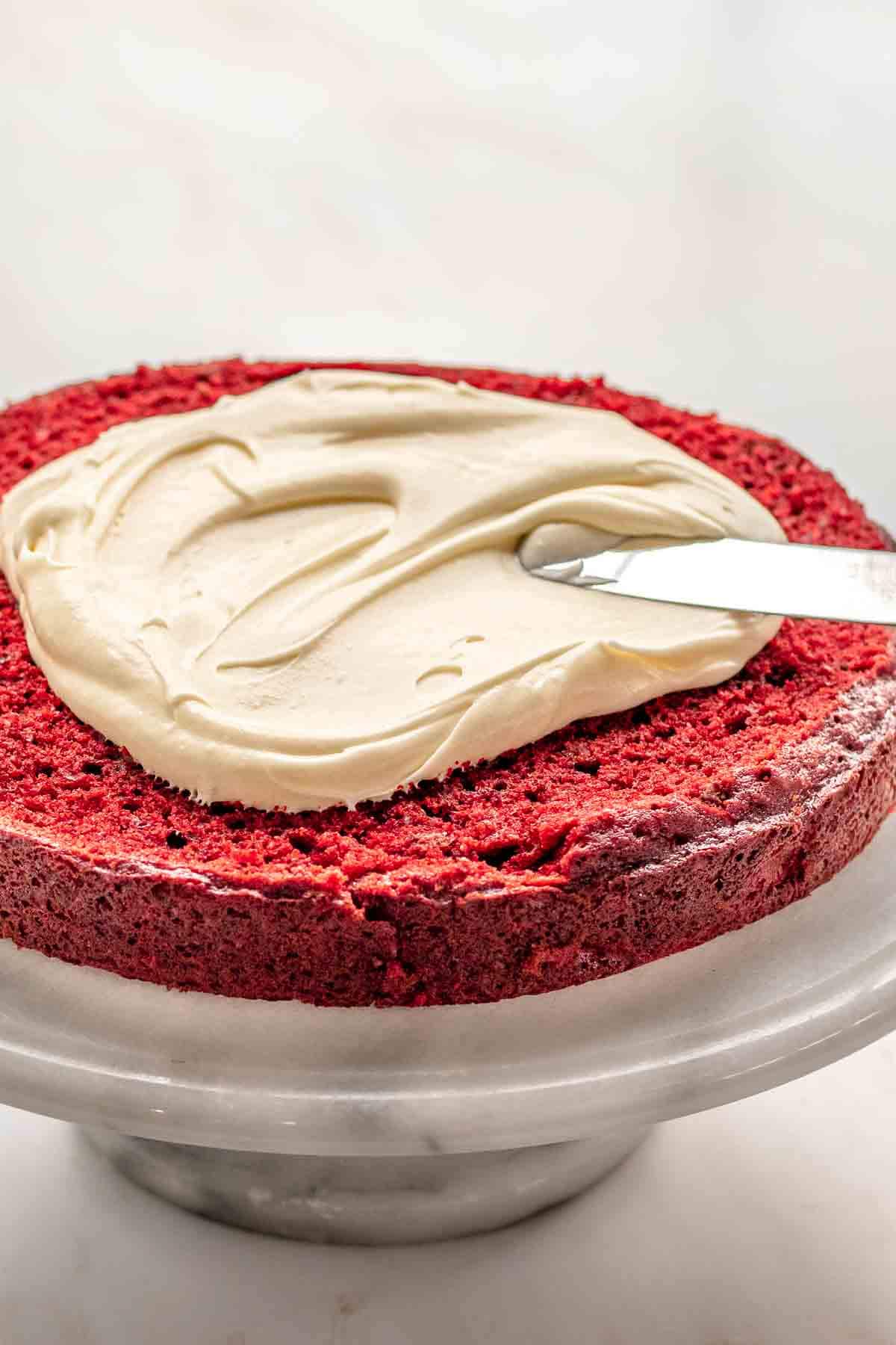 Red Velvet Cheesecake Cake spreading frosting on first cake layer on cake stand