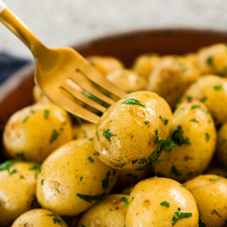 Butter Steamed Baby Potatoes close up of potato on fork over cooked and garnished potatoes in bowl