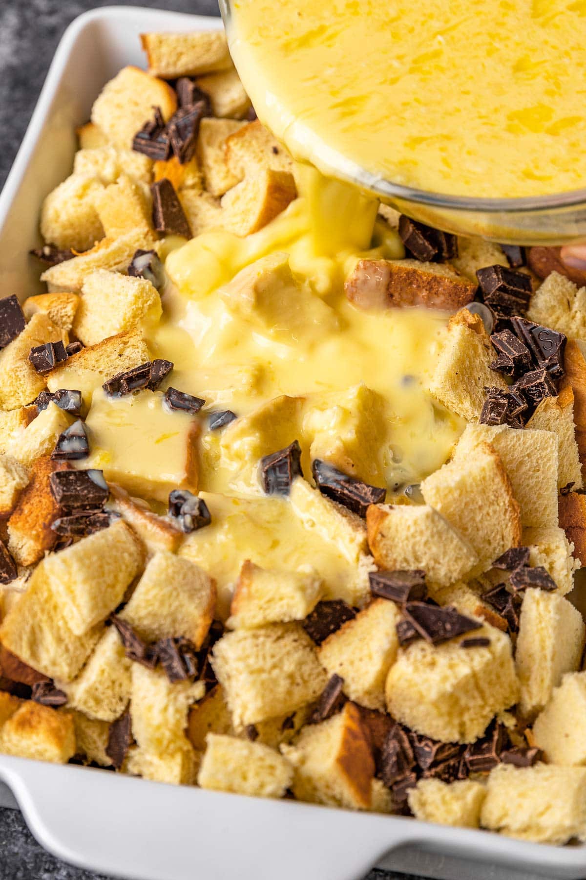 Dark Chocolate Bread Pudding pouring custard over layered bread pudding in pan