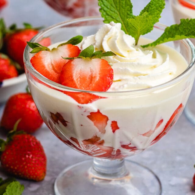 Cream with strawberries in glass chalice with whipped cream, mint and berry garnish