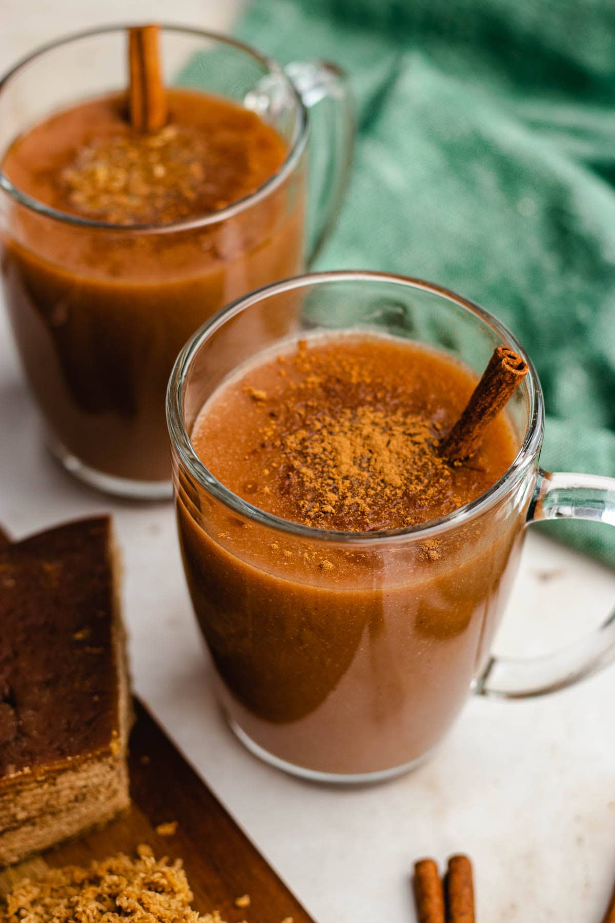 Mexican Atole finished in two glass cups with cinnamon sticks. Piloncilo brick next to cup