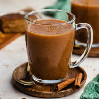 Mexican Atole finished in cup on brown plate, cinnamon sticks and spoon on plate, 1x1