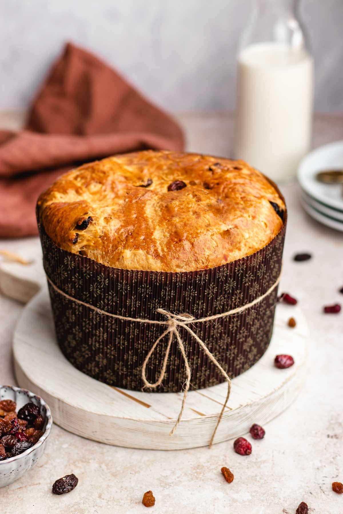 Panettone baked loaf in brown paper mold with string wrapped around the middle, foreground decorated with mixed fruit and nuts