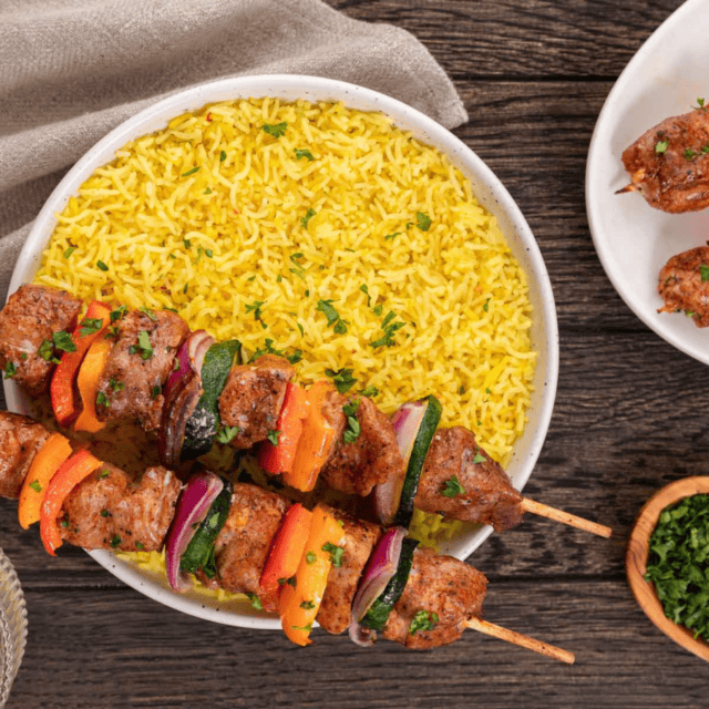 bowl of yellow rice with kebobs on top