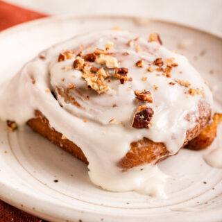 Sweet Potato Cinnamon Roll on plate baked with frosting and pecans, 1x1 size