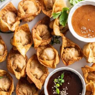 close up of Sauce in white bowls with wontons on a white serving platter.