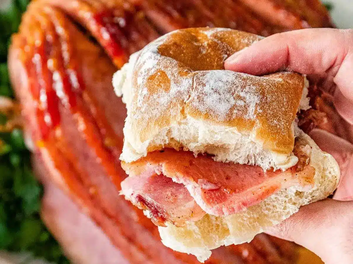 Piece of ham on a roll being held by a hand