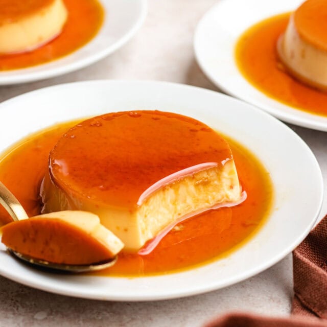 Creme Caramel finished custard covered in caramel on plate with spoon. Portion of creme caramel missing with that portion on spoon. 1x1