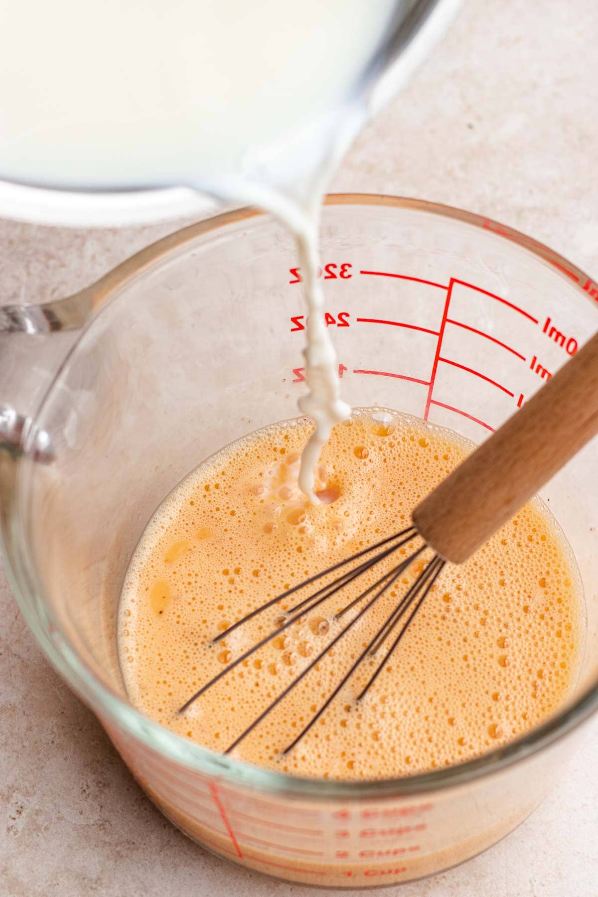 Creme Caramel tempering milk and egg mixture in large glass measuring cup with whisk.