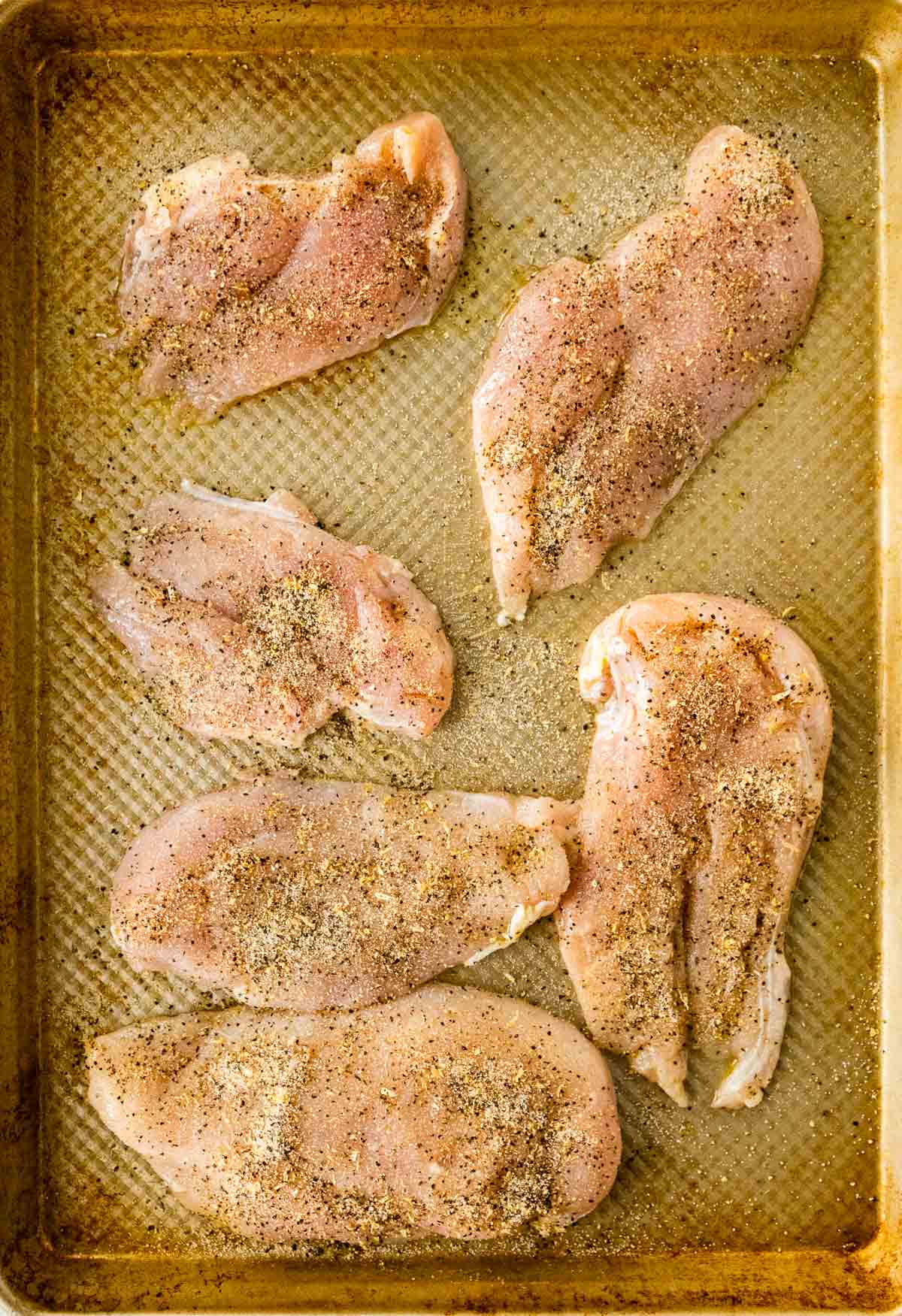 raw seasoned chicken on baking sheet