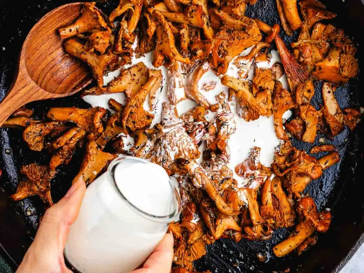 Cream being poured into pan with sliced mushrooms.