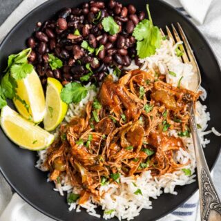 Beef served on black plat with rice, beans, and lime, with fork