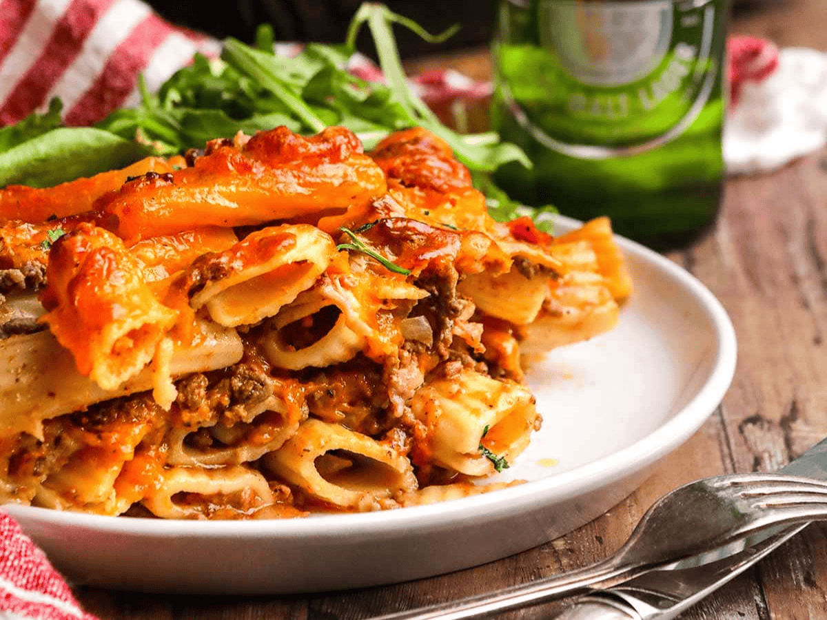 plated ziti on a table with beer in the back