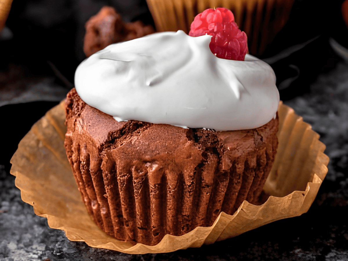 brown chewy dessert in a muffin liner with cream on top with a raspberry