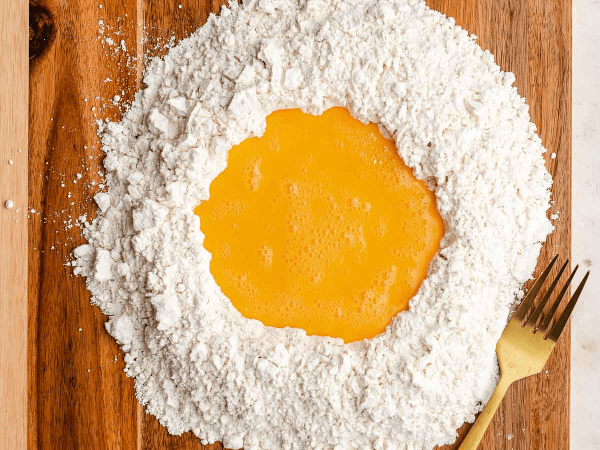 Mound of flour with egg mixture in center.