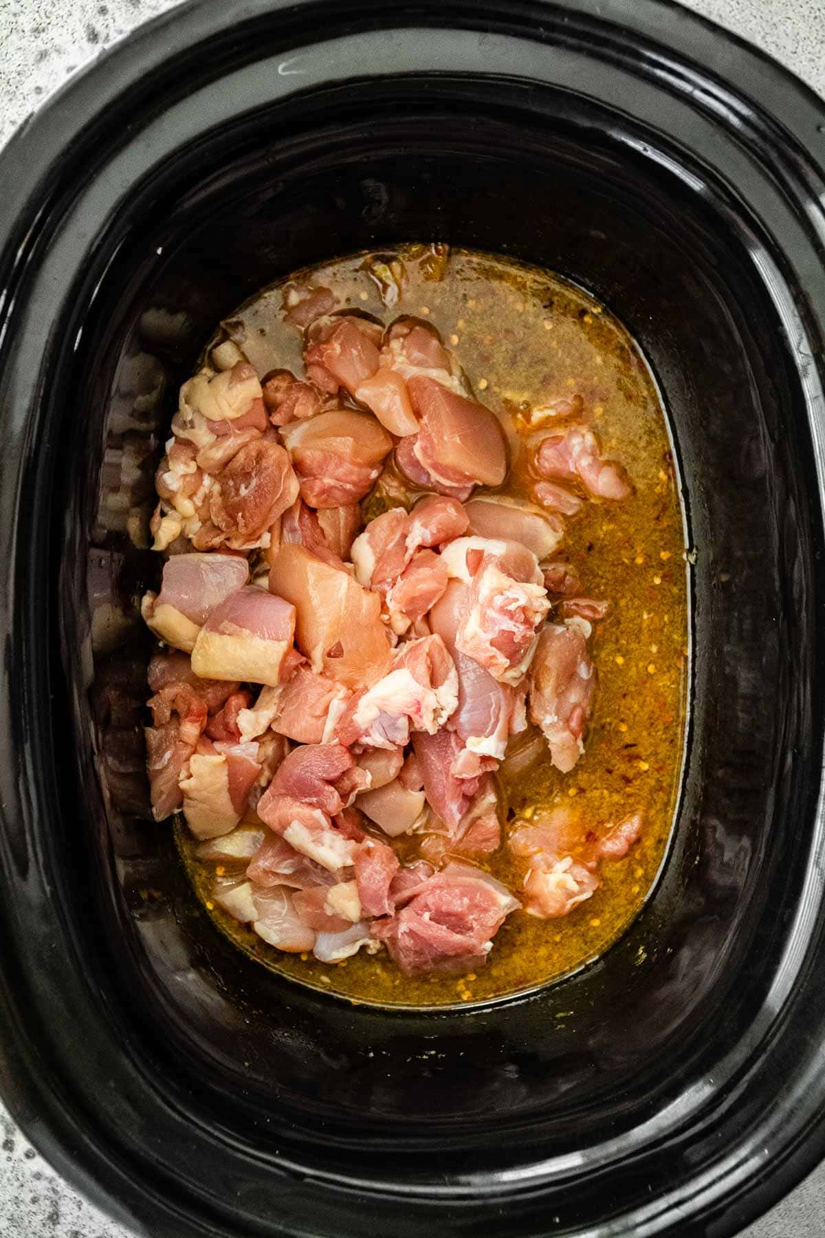 Slow Cooker Orange Chicken raw chicken pieces in slow cooker with sauce