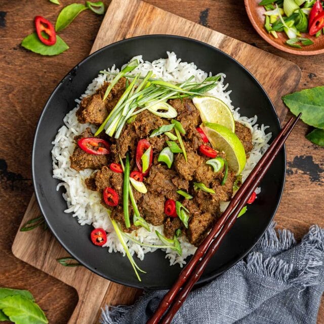Beef Rendang cooked in black bowl over bed of steamed rice with chopsticks on bowl, 1x1