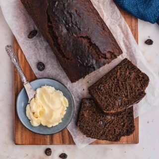 Boston Brown Bread baked on parchment paper covered cutting board with cut slices and butter, top down view, 1x1