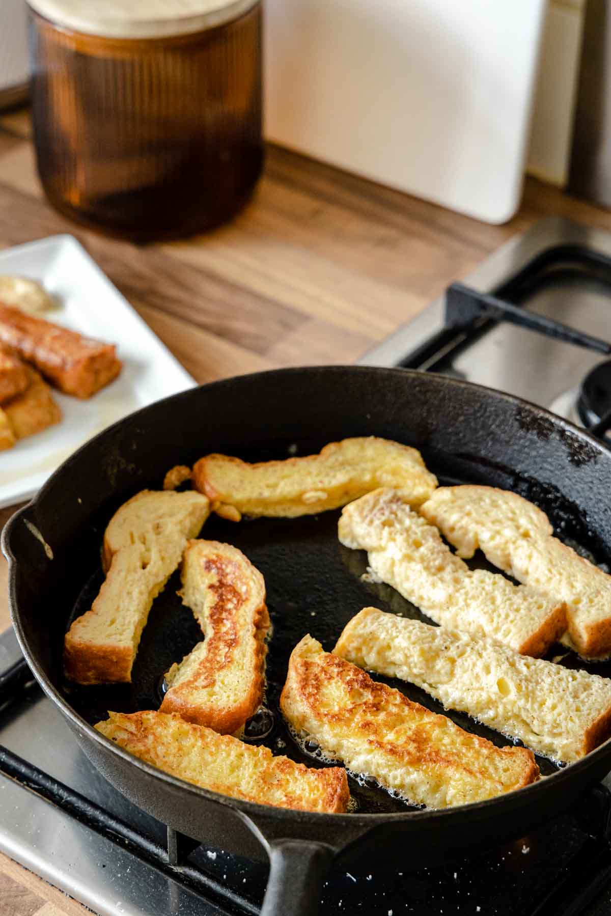 French Toast Sticks cooking sticks in a cast iron skillet after flipping