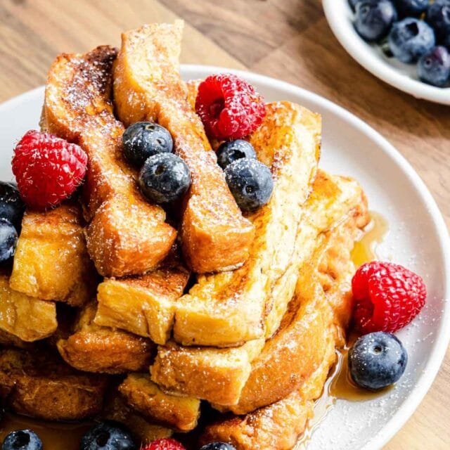 French Toast Sticks finished, stacked on a plate with berries and syrup, 1x1