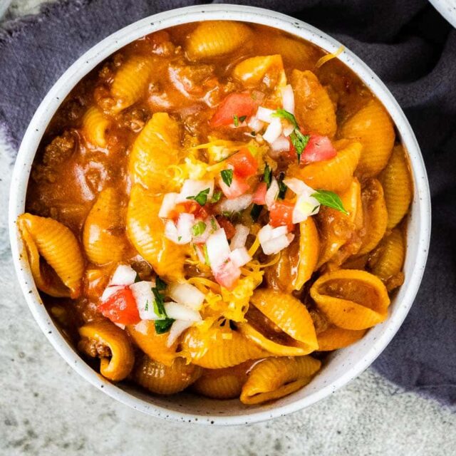macaroni shells covered in melted dairy and ground meat in a bowl with garnish