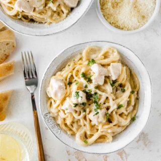 Instant Pot Chicken Alfredo finished pasta in bowl, bowl of parmesan cheese and fork near bowl, 1x1