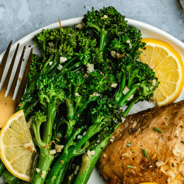 Green Vegetables on a white plate with lemons and chicken with a gold fork