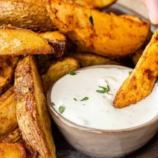 closeup of cooked potatoes with dipping a wedge into ranch