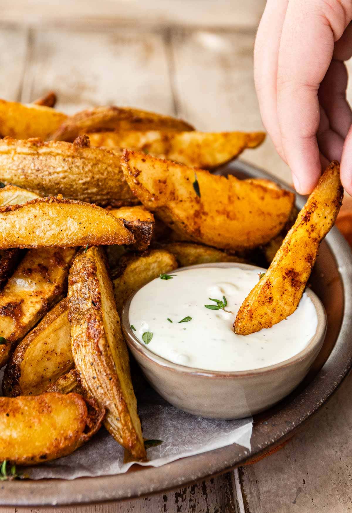 closeup of cooked potato wedges with dipping a wedge into ranch