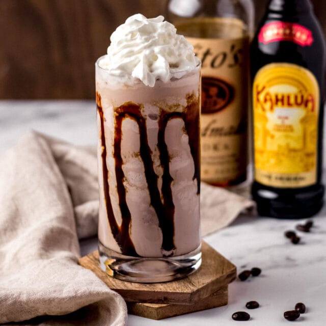 TGI Fridays Mudslide finished milkshake in glass with chocolate syrup in glass and whipped cream on top, alcohol bottles in background, 1x1