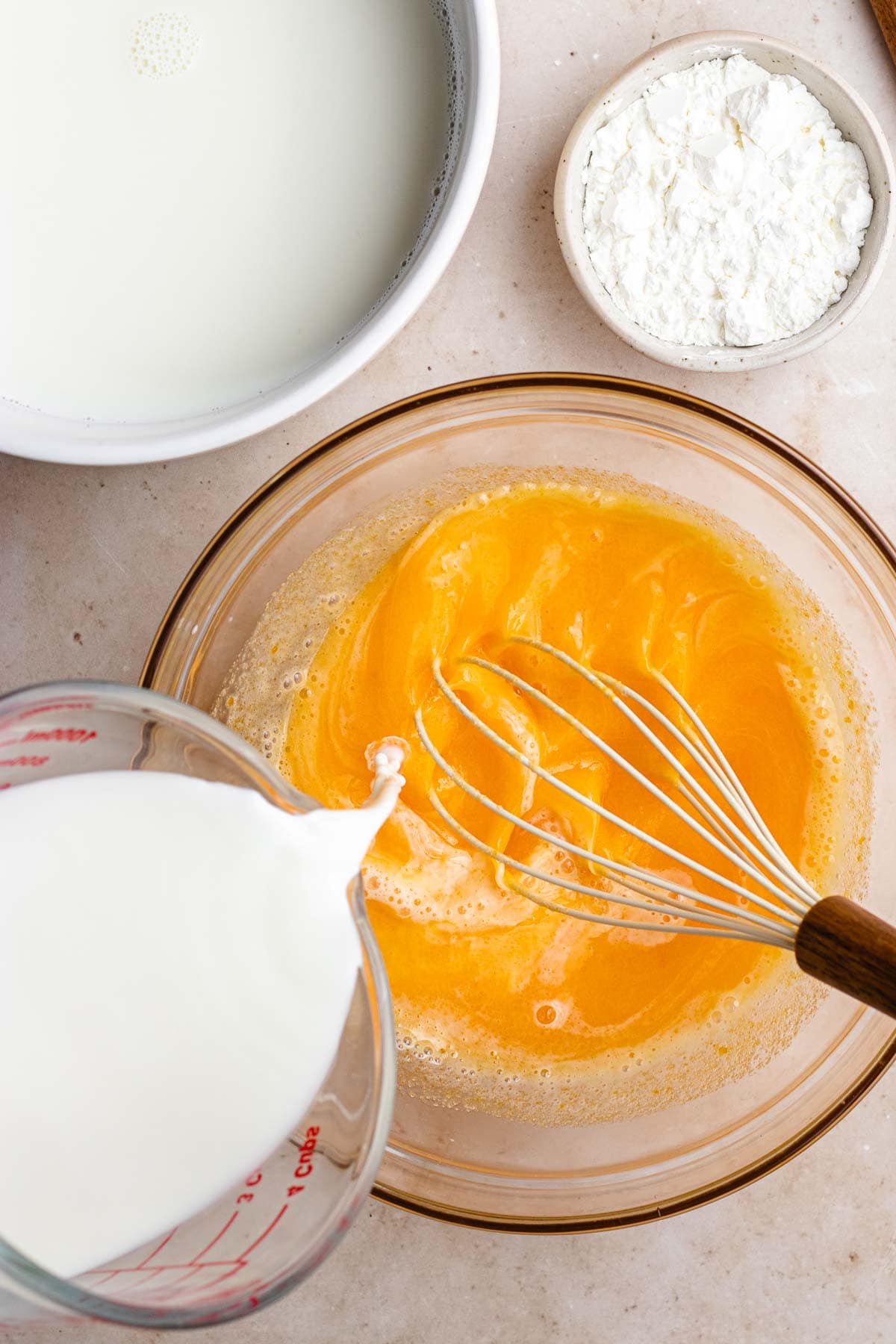 Vanilla Pudding adding milk to whisked eggs yolks in glass bowl with whisk
