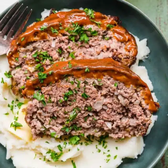 sliced meatloaf on top of mashed potatoes on a plate