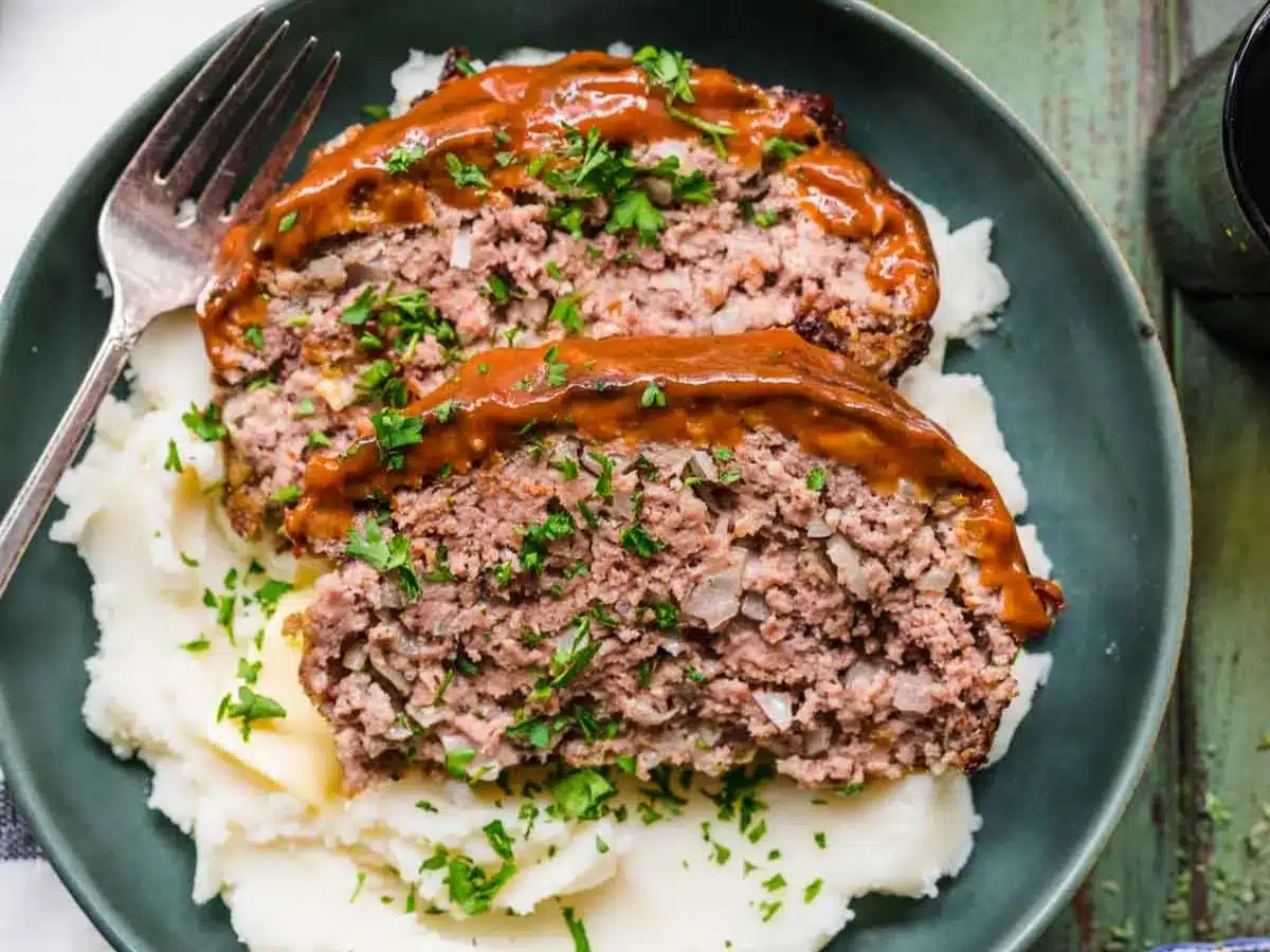 sliced meatloaf on top of mashed potatoes on a plate