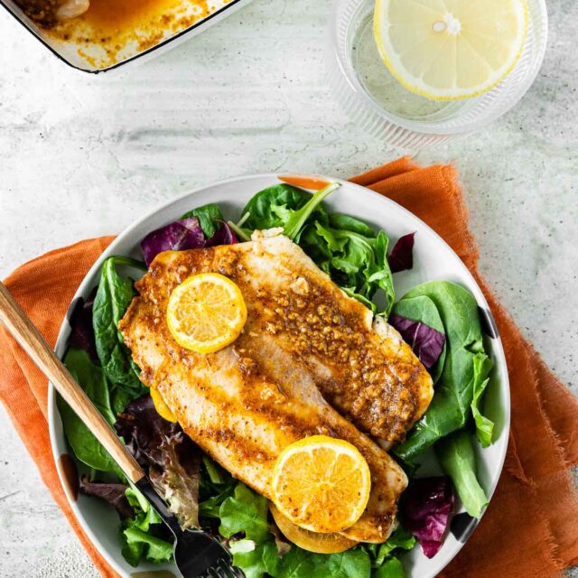 baked tilapia on bed of salad with two lemon slices
