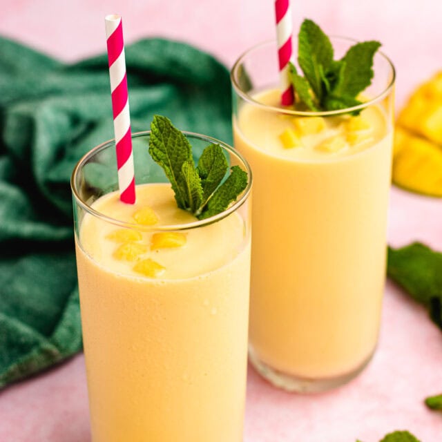 Mango Smoothie two glasses filled with mango smoothie with red striped straw and garnished with mint. 1x1